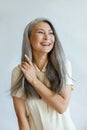 Middle aged Asian woman touches natural hoary hair on light grey background