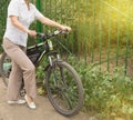 Middle-aged attractive slim woman in light trousers and shirt stands near the bike in the Park on a Sunny summer day, Cycling Royalty Free Stock Photo