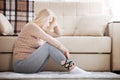 Middle aged barefoot woman sitting at the floor embracing her knees, near sofa at home, her head down, bored, troubled Royalty Free Stock Photo