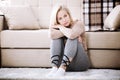 Middle aged barefoot woman sitting at the floor embracing her knees, near sofa at home, her head down, bored, troubled Royalty Free Stock Photo