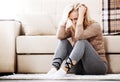 Middle aged barefoot woman sitting at the floor embracing her knees, near sofa at home, her head down, bored, troubled Royalty Free Stock Photo