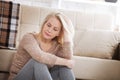 Middle aged barefoot woman sitting at the floor embracing her knees, near sofa at home, her head down, bored, troubled Royalty Free Stock Photo