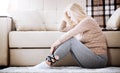 Middle aged barefoot woman sitting at the floor embracing her knees, near sofa at home, her head down, bored, troubled Royalty Free Stock Photo