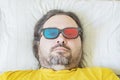 A middle-aged bearded man lies on a pillow in the early morning in colored 3D glasses Royalty Free Stock Photo