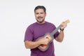 A middle aged bearded man playing the ukelele. Strumming a small guitar. Isolated on a white background