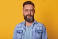 Middle aged bearded smiling calm man standing isolated over bright yellow background, looking directly at camera, wearing casual