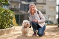 Middle-aged blond woman walking with fluffy white dog in summer city