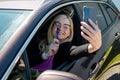 Middle aged blonde woman in glasses making selfie with a smartphone through an open car window Royalty Free Stock Photo