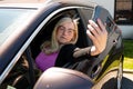 Middle aged blonde woman in glasses making selfie with a smartphone through an open car window Royalty Free Stock Photo