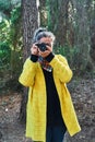 Woman makes photos with analog reflex camera looking at camera in forest