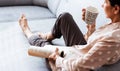 Middle-aged brunette woman on the gray sofa reading book with cup of coffee, soft focus, stay at home concept, cozy background Royalty Free Stock Photo