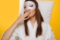 Brunette woman lies on pillow with sleeping mask over her eyes, yawning Royalty Free Stock Photo