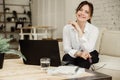 Middle aged business woman working at home using laptop, smiling and looking at the camera