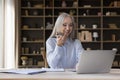 Middle-aged businesslady talks on speakerphone seated at desk with laptop Royalty Free Stock Photo