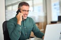 Middle aged businessman making call on cell phone using laptop in office. Royalty Free Stock Photo