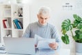 Middle aged businessman reading paper documents and using laptop while working at home office. Confident, experienced Royalty Free Stock Photo