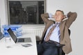 Middle-aged businessman resting on chair in front of laptop in office