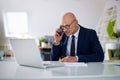 A middle-aged businessman is sitting in his office and using laptop and smartphone for work Royalty Free Stock Photo