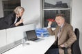 Middle-aged businessman throwing paper airplane towards female colleague in office Royalty Free Stock Photo