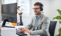 Middle aged businessman using a headset and computer in a modern office Royalty Free Stock Photo