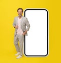 Middle aged businessman wearing casual white suit leaned on huge giant smartphone with white screen smiling looking at Royalty Free Stock Photo