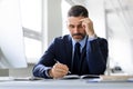 Middle aged businessman writing in notepad, sitting at desk in office interior, free space Royalty Free Stock Photo