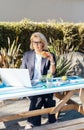 Middle-aged businesswoman having lunch at the park outdoor cafe, picnic area and working on laptop during her break Royalty Free Stock Photo