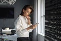 Businesswoman standing at the office by the window and using mobile phone