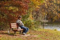 A middle aged caucasian man wearing jeans and sneakers is sitting alone on a bench feeding pigeons.