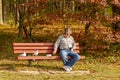 A middle aged caucasian man wearing jeans and sneakers is sitting alone on a bench feeding pigeons.