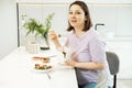 Middle aged woman eating noodles with chopsticks, holding paper box at home in kithcen