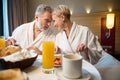 Middle aged couple having breakfast and looking at each other on bed at table Royalty Free Stock Photo