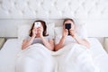 Middle aged couple hold mobile phones in bedroom, modern people concept
