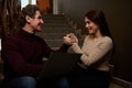 Middle-aged couple with a laptop, sitting on stairs, holding hands and spending nice time during coffee break in a hallway of a Royalty Free Stock Photo