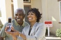 Middle-aged couple photographing in front of new home Royalty Free Stock Photo