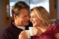 Middle Aged Couple Sitting On Sofa With Hot Drinks Royalty Free Stock Photo