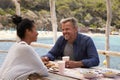 Middle aged couple sitting at table by the sea looking away Royalty Free Stock Photo