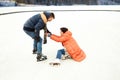 Middle-aged couple skating on open air ice rink. Man helping fallen woman to get up. Concept of leisure activity, winter