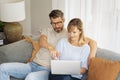 Middle-aged couple wearing casual clothes and sitting at home on the sofa and using a laptop Royalty Free Stock Photo