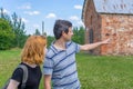 Middle aged dark-haired tourist man showing direction by hand for young redhead lady. Traveler asking path from stranger on