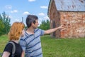 Middle aged dark-haired tourist man showing direction by hand for young redhead lady. Traveler asking path from stranger on