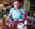 Middle aged European man drinks coffee with dessert in restaurant