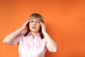 Middle aged european woman holding her head, orange background, concept headache, stress, close-up, copy space