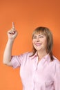 Middle aged european woman standing, showing upstairs, orange background, close-up, copy space