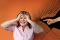 Middle-aged European woman stands protestingly extending both hands, cracks, male hand shows an accusatory finger, orange