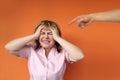 Middle aged european woman stands protestingly extending both hands, male hand shows finger accusatory, orange background, close-