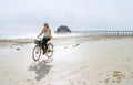 Middle-aged female dressed light summer clothes riding old vintage bicycle with front basket on the lonely low tide ocean white Royalty Free Stock Photo