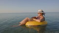 Middle aged female working on laptop computer in orange inflatable life ring on vacation