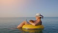 Middle aged female working on laptop computer in orange inflatable life ring on vacation