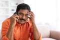 Middle aged hindu man sitting on couch, have phone conversation Royalty Free Stock Photo